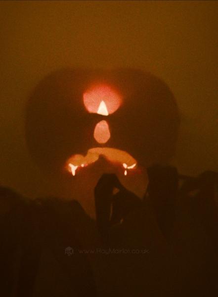 A close-up 3D render of a large, glowing, pumpkin-headed figure reaching towards the viewer from a misty orange landscape.